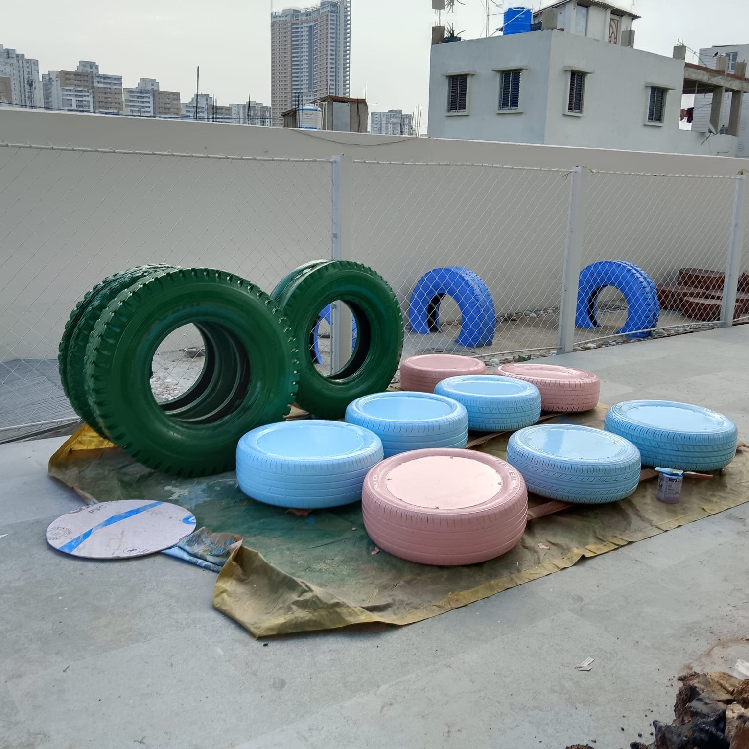 Painted tyres in green, blue, and pink drying on rooftop